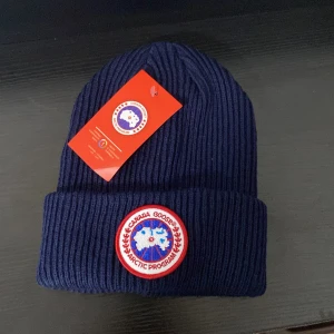 Marinblå ribbad mössa  - Snygg marinblå ribbstickad mössa med klassisk rund patch framtill i vitt, rött och blått. Mössan har uppvikt kant och är tillverkad i mjukt stickat material som håller dig varm. Perfekt för kalla dagar och har en clean, stilren look.