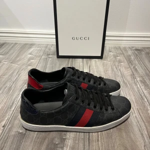 Gucci Ace svarta sneakers med röd/blå detalj - Riktigt snygga Gucci ace dojor i strl 42. De ser helt nya ut förutom små slitningar på insidan av skon, vilket man inte ens ser. Box medföljer. Hör av dig vid frågor.