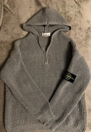 Unik Grå stickad hoodie från Stone Island S/M - Säljer en grå stickad hoodie från Stone Island med ribbad struktur och klassisk logotyp-patch på ärmen. Tröjan har huva, lång ärm och en snygg half zip-dragkedja framtill. Perfekt för dig som gillar streetwear och vill ha något både stilrent och bekvämt. Skriv privat om ni har några frågor angående tröjan och kan givetvis skicka flera bilder & tröjan har använts 2gånger. Fraktar inom 24h ;) 