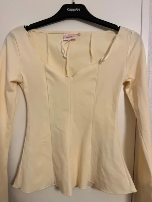 Ljusgul långärmad topp Gina Tricot - Supersöt ljusgul långärmad topp från Gina Tricot med figurnära passform och markerad midja. Toppen har en snygg v-ringad skärning framtill och är tillverkad i ett mjukt, stretchigt material som sitter bekvämt. Perfekt att styla med jeans eller kjol.