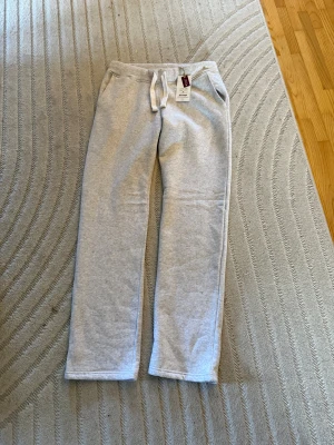 Ljusgrå mjukisbyxor med snörning L - Ljusgrå mjukisbyxor från Russemerch i storlek L. Byxorna har dragsko i midjan, raka ben och mjukt material som känns skönt mot huden. Perfekta för chill dagar eller när du vill vara extra bekväm. Klassisk look med fickor på sidorna.