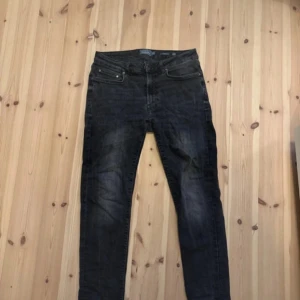 Svarta jeansbyxor från dressman - Säljer ett par svarta jeansbyxor från dressman  med klassisk femficksdesign och smal passform. Jeansen har en mörk tvätt med lätt slitna detaljer och dragkedja i gylfen. Perfekt för dig som gillar en stilren och enkel look.