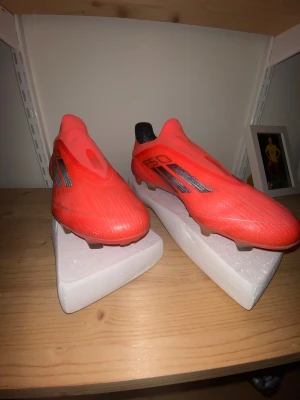 Adidas F50 elite - Säljer ett par Adidas F50 Ag elite fotbollsskor i en riktigt fet röd färg med svarta detaljer och silvriga Adidas-loggor på hälen. Skorna har en strömlinjeformad design utan snörning och är gjorda i syntetmaterial för maxad känsla på planen.
