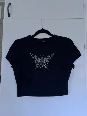 Svart croppad topp med strass-fjäril - Svart croppad topp som har en stor fjäril i silvriga stenar. Mjuk bomull med lite stretch, perfekt till jeans eller kjol. Sitter lite tightare och framhäver midjan 💕 Köper du innan kl 16:00 kan jag posta samma dag!