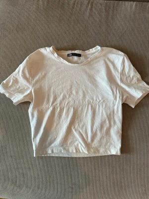 Vit croppad topp från Zara - En stilren vit croppad topp från Zara med rund halsringning och korta ärmar. Tillverkad i mjuk bomull som känns skön mot huden. Enkel design som är lätt att matcha med olika outfits. Perfekt för dig som gillar minimalistisk stil.