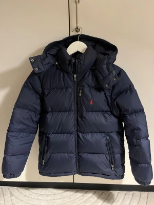 Mörkblå pufferjacka Polo Ralph Lauren - Snygg Ralph Lauren vinter jacka! Säljer pga den blivit för liten. Lite smink defekter vid kragen, ska prova att tvätta. Tyvärr står även mitt namn samt nummer på lappen innuti jackan, men det tänker man inte på samt går att stryka över! Köpt på kidsbrandstore, storlek L(ålder 14-16) och sitter som en XS.  Nypris 3295❤️ Skriv gärna vid frågor!