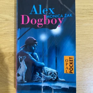 Alex Dogboy - En pocketbok med ett fängslande omslag som visar en ung person och två hundar i en stadsmiljö. 