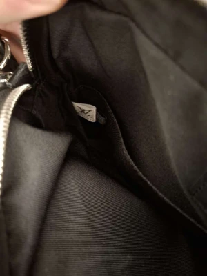 Louis Vuitton svart axelväska i skinn - Snygg svart axelväska från Louis Vuitton med klassiskt monogrammönster. Väskan har justerbar axelrem med logotyp, flera fack med dragkedja och en avtagbar mindre ficka framtill. Tillverkad i skinn med mörka detaljer och stilren design.