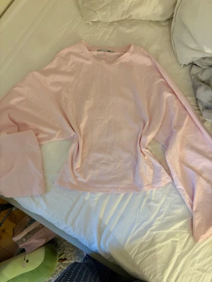 Ljusrosa långärmad tröja med vida ärmar - Säljer en ljusrosa långärmad tröja med riktigt breda och vida ärmar. Tröjan har en enkel rund halsringning och är gjord i mjuk bomull som känns skön mot huden. Perfekt för dig som gillar en chill och unik stil.