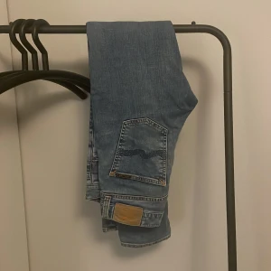 Blå jeans från Nudie Jeans Co - Ett par klassiska blå jeans från Nudie Jeans Co med snyggt slitna detaljer och broderad bakficka. Jeansen har slim passform och är tillverkade i mjukt denimtyg. Tidlösa skulle jag säga. Modellen är Lean Dean storlek 28/32 men sitter som 29/32. De är använda under 5 gånger och priset är inte hugget i sten. Skriv vid minsta fundering.
