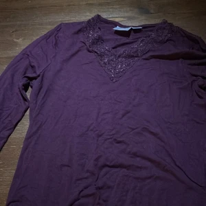 Vinröd långärmad topp med spets Gina Tricot - Vinröd långärmad topp från Gina Tricot med snygg v-ringning och dekorativ spets runt halsen. Mjuk och skön känsla, perfekt att styla med jeans eller kjol. Färgen är djup vinröd och spetsen ger en extra detalj till looken.