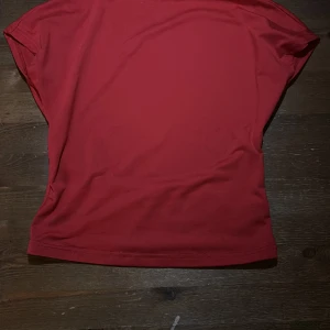 Röd topp med öppen rygg - Säljer en röd topp med korta ärmar och en riktigt snygg öppen rygg. Toppen har en enkel, clean design framtill och är tillverkad i ett mjukt, stretchigt material som känns skönt mot huden. Perfekt för dig som vill sticka ut lite extra med en cool detalj i ryggen. Bara testat 