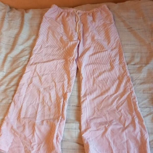 Randiga byxor med snörning - Luftiga och bekväma byxor med rosa och vita smala ränder. Byxorna har resår i midjan och snörning. 