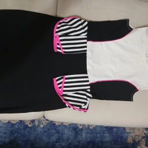 Svartvit randig klänning LC Waikiki - Snygg svart och vit klänning från LC Waikiki med coola svarta och vita ränder och rosa detaljer vid midjan. Klänningen har kort ärm, figurnära passform och knapp i nacken. Perfekt för dig som gillar en unik och färgstark stil.