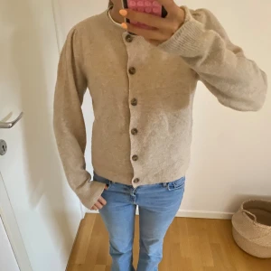 Beige kofta med knappar - Mysig beige kofta med rund hals och bruna knappar framtill. Koftan har långa armar med lite puff vid axlarna och är stickad i ett mjukt material. Pris kan dissekeras🤗🤎