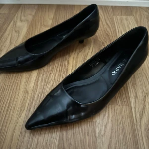 Svarta pumps från Primark med spetsig tå - Klassiska svarta pumps från Primark med spetsig tå och låg klack. Skorna har en stilren och enkel design i syntetmaterial med glansig finish. 