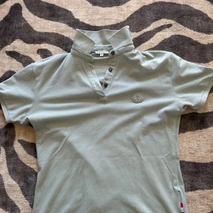 Ljusgrön Moncler t-shirt med krage - Snygg ljusgrön t-shirt från Moncler med korta ärmar, uppvikbar krage med logga och knappslå framtill. Klassisk Moncler-logga på bröstet. Tillverkad i mjuk bomull för en skön känsla och clean look.