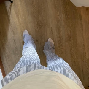 Randiga pyjamasbyxor med snörning - Säljer ett par lösa och bekväma pyjamasbyxor med blåvita ränder och snörning i midjan. Byxorna har en relaxed fit och är perfekta för chill dagar hemma. Tillverkade i mjukt bomullstyg för extra komfort.