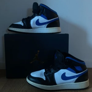 Nike Air Jordan 1 Mid svart/blå/vit - Säljer ett par Nike Air Jordan 1 Mid med svart, blå och vit färgkombination. Skonsamt använda, sko box medföljer. Super snygga och bekväma skor!