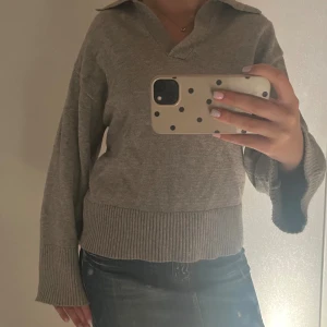 grå stickad tröja från Gina Tricot - Säljer en grå stickad tröja från Gina Tricot i storlek XS. Tröjan har v-ringning, krage och breda ribbade muddar vid ärmslut och nederkant. Perfekt för lager-på-lager och har en avslappnad, loose passform💕