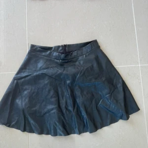 Svart kortkjol i skinnimitation H&M - Snygg svart kortkjol från H&M i skinnimitation. Kjolen har en lätt utsvängd form och dragkedja bak. Perfekt för dig som vill ha en edgy och trendig look. Passar till många olika stilar och är enkel att matcha med både sneakers och boots.