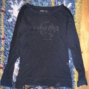 Svart långärmad Hard Rock Cafe-tröja - Svart långärmad tröja från Hard Rock Cafe London med stenar på bröstet. Tröjan har en avslappnad passform och är tillverkad i mjuk bomull. Perfekt för dig som gillar ikoniska tryck och vill ha en cool vardagsstil.