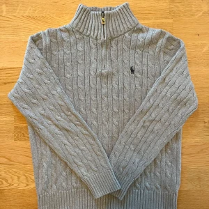 Grå Ralph lauren halv zip - säljer en snygg grå Ralph lauren halv zip som är kabelstickad, den har inga defekter och är i väldigt bra skick. Den är storlek 14-16 år som motsvarar xs, den passar runt 160-165. priset är inte hugget i sten.