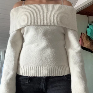 Offshoulder vit stickad tröja - Superfin offshoulder stickad tröja i vitt med bred ribbad kant upptill och vid midjan. Tröjan har lång ärm och sitter snyggt på axlarna. Perfekt för dig som vill ha en mysig men ändå stilren look.