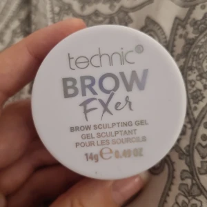 Technic Brow FXer Brow Sculpting Gel - Technic Brow FXer är en genomskinlig bryngel i rund plastburk, 14g. Perfekt för att forma och fixera brynen med en fluffig, fjäderlätt finish. Vegansk formula. Locket är vitt med silver- och grå text. Enkel att ta med i sminkväskan.