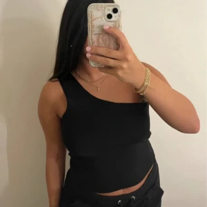 Svart one shoulder topp - Snygg svart topp med one shoulder-design och croppad passform. Perfekt för dig som gillar en stilren och trendig look. Toppen är ärmlös och har en tight siluett som framhäver figuren.