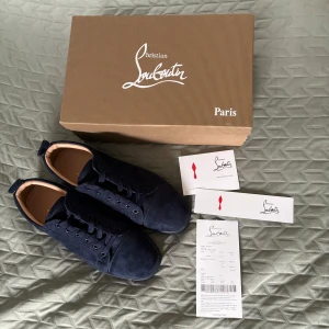 Mörkblåa mocka Christian Louboutin skor strlk 43 - Snygga mörkblå sneakers från Christian Louboutin i lyxig mocka med ton-i-ton snörning och diskret broderad logga på hälen. Skorna har en klassisk rund tå och svart sula, samt mjukt beige innerfoder i skinn för extra komfort. Perfekta för dig som gillar stilrena och exklusiva sneakers.