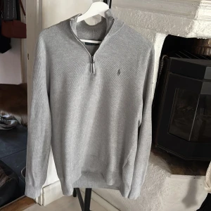 Grå half zip tröja Polo Ralph Lauren - Snygg grå långärmad tröja från Polo Ralph Lauren med half zip och diskret broderad logga på bröstet. Tröjan är stickad i bomull och har en klassisk passform med ribbade muddar och krage. Perfekt för lager-på-lager under höst och vinter köpte på nk i juli för 2400 och har använt kanske bara 4-5 gånger 