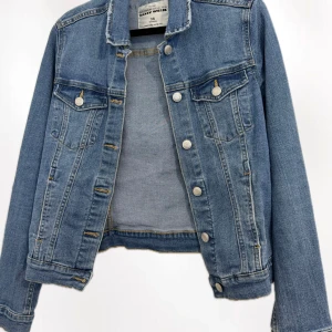 Blå jeansjacka från Tally Weijl - Snygg klassisk blå jeansjacka från Tally Weijl i storlek 36. Jackan har silverfärgade knappar framtill och på bröstfickorna, samt långa ärmar och coola sömdetaljer. Perfekt att slänga över en hoodie eller t-shirt för en chill look.
