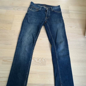 Nudie Jeans grim tim blå jeans W29 L30 - Snygga blå jeans från Nudie Jeans med klassisk femficksdesign och orangea sömmar på bakfickorna. Jeansen har en rak passform och är tillverkade i slitstarkt denim. Perfekt skick inga alls defekter. Kontakta vid frågor, priset är inte hugget i sten! Dvs kommer inte acceptera orimliga summor men har vi en bra konversation kan det prutas ner LITE. 