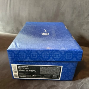 Bearbrick Clot x Nike  - Bilderna visar en samlarleksak från BE@RBRICK CLOT x Nike, med två figurer i en snygg blå box. Det är ingen bok, utan en designad figur som passar perfekt för dig som gillar streetwear, konst och unika samlarobjekt. Perfekt för att ge din hylla eller skrivbord en cool vibe.