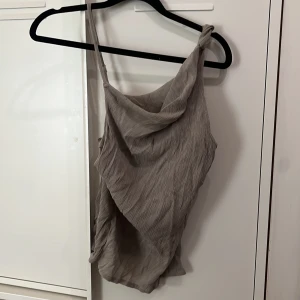 Beige  linnetopp från Weekday - Säljer en beige linnetopp från Weekday i storlek S. Toppen har en snygg omlott-design med draperad framsida och smala axelband, varav det ena är knutet. Materialet är lätt och har en skrynklig struktur som ger en cool look.