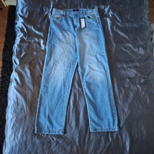 ADPT ljusblå baggy jeans, strl 32 - Säljer ett par ljusblå baggy jeans från ADPT i modellen Malcolm. Jeansen har klassisk femficksdesign, raka ben och är tillverkade i denim. Perfekta om du gillar en avslappnad och loose fit-stil. Färg: light blue denim.