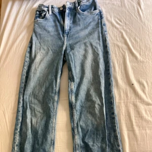 Blå wide jeans från H&M, hög midja - Säljer ett par ljusblå jeans från H&M med wide fit och hög midja. Jeansen har justerbar midja, klassisk femficksdesign och raka ben. Är lite skrynkliga på bilden men går att fixa 