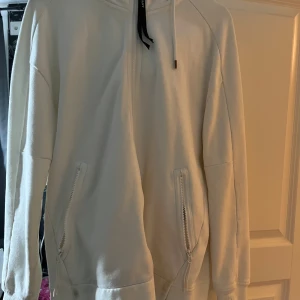 Vit hoodie med goggles från C.P. Company - Säljer en vit hoodie från C.P. Company med hel dragkedja, två fickor med dragkedja och ikoniska goggles i huvan. Tröjan har långa ärmar, snörning i huvan och en clean, oversized look. Perfekt för dig som vill sticka ut med streetwear-vibe. Storlek L.