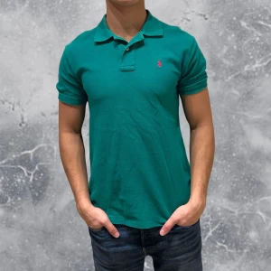 Ralph Lauren Piké grön  - •Ralph Lauren Piké Grön. Skick: 8/10, Inga skador. Storlek: 14/16 år~160-170 cm). Modell: 174 cm, 63 kg (sitter bra på modellen på bild). Authentic: ✅. Hör av dig vid frågor eller funderingar, mvh Hessler’s;)