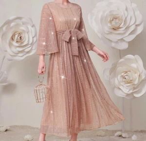 Glittrig champagnefärgad långklänning - Oanvänd långklänning i champagnefärg med glittriga detaljer och breda trekvartsärmar. Klänningen har ett markerat midjeband med stor rosett framtill. Pris kan diskuteras!