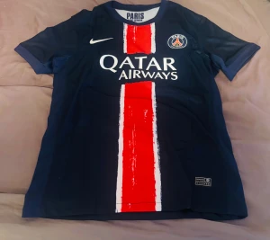 PSG O.Dembélé #10 Nike fotbollströja - Snygg PSG matchtröja med O.Dembélé och nummer 10 på ryggen. Marinblå med en bred röd och vit rand på framsidan, Paris Saint-Germain klubbmärke och Nike-logga. Qatar Airways tryck på bröstet. Tillverkad i lätt och ventilerande polyester. EJ ORIGINAL!