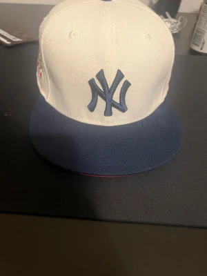 New Era Yankees World Series keps - Snygg New York Yankees keps från New Era med broderad World Series-logga på sidan. Kepsen är vit med mörkblå skärm och detaljer, samt klassiskt NY-logo framtill. Tillverkad i bomull och har MLB-logga bak. Perfekt för dig som gillar sportig streetstyle.