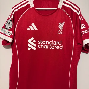 LIVERPOOL HEMMATRÖJA 2025/26 - Liverpools hemmatröja säsongen 2025/26. Smal passform. Tröjan tillverkad med AEROREADY-teknik. Det innebär att den tillverkas i fukttransporterande material som säkerställer optimal ventilation under hela träningspasset.