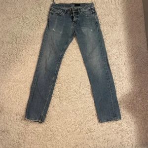 Blå jeansbyxor Alex 29/32 - Snygga blå jeansbyxor från Alex i modellen PRG-Feral Blue. Klassisk femficksdesign, raka ben och normal passform. Jeansen har slitna detaljer. 3 st hål men syns inte så mycket. 