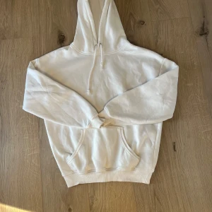 Vit hoodie från BikBok XS - Säljer en clean vit hoodie från BikBok i storlek XS. Tröjan har huva med snörning, ribbade muddar och en stor magficka. Perfekt för chill dagar och enkel att matcha med jeans eller leggings.