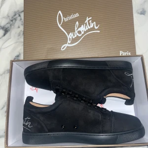 Svarta sneakers Christian Louboutin - Säljer ett par svarta sneakers från Christian Louboutin i mocka med signaturbroderi på hälen och klassisk röd sula. Skorna har rund tå, snörning och platt sula. Snygg och stilren design som sticker ut med den röda undersidan och exklusiva detaljer. Använd en gång inga tecken på användning, pris kan diskuteras.