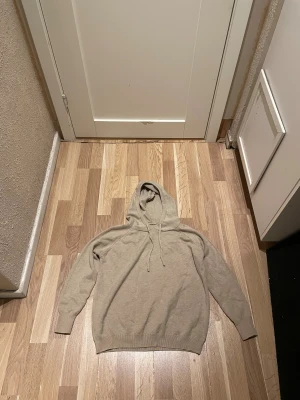 Beige merinoulls hoodie med snörning storlek S - Snygg beige hoodie med huva och snörning storlek S.Tröjan har långärmade ärmar och ribbade muddar vid ärmslut och nederkant. Perfekt för chill dagar och enkel att matcha med jeans eller joggers.