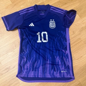 Argentina Messi #10 fotbollströja Adidas - Snygg Argentina fotbollströja från Adidas med Messi och nummer 10 på ryggen. Tröjan är mörkblå med lila detaljer och har ett grafiskt mönster framtill. Kortärmad modell i lätt och ventilerande polyester, perfekt för match eller träning.