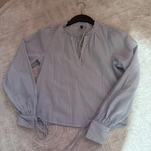 Blå blus från H&M - En blå fin blus med snören vid halsen och armarna fin och lite lätt  randig 